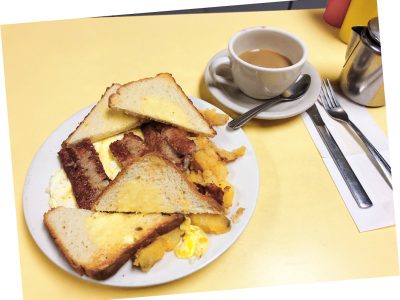 2 Eggs Any Style Platter. This picture D pics a platter with scrambled eggs home fried potatoes and sliced toast on top of a white platter served on Johnny’s yellow counter. It also shows a side order of sausage that is usually an additional charge