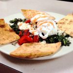 Aidans Way. This picture did pics two poached eggs served on top of a bed of sautéed spinach and roasted peppers, accompanied with a toasted pita cut into four triangular pieces on top of a plate Served on Johny’s original white counter