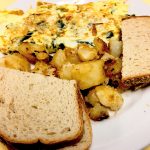 Florentine Omelette. This picture depicts the omelette that consists of spinach and feta cheese accompanied by home fried potatoes and toast served on a white platter on Johnys counter top