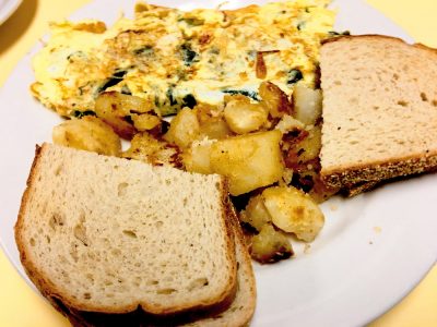 Florentine Omelette. This picture depicts the omelette that consists of spinach and feta cheese accompanied by home fried potatoes and toast served on a white platter on Johnys counter top