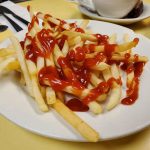 French Fries. This picture shows an order of shoestring french fries topped with ketchup served on a white platter on Johnny’s yellow countertop. With a cuppa coffee on the side for an extra charge
