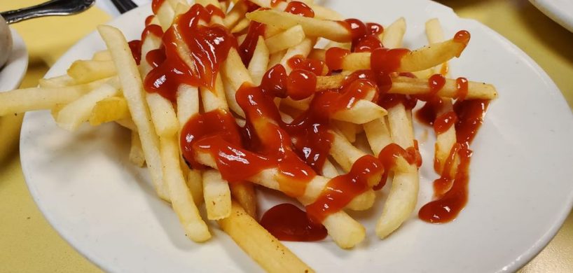 French Fries. This picture shows an order of shoestring french fries topped with ketchup served on a white platter on Johnny’s yellow countertop. With a cuppa coffee on the side for an extra charge