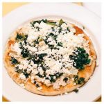 Great Alexander. This picture depicts an order of fresh tuna salad that is topped with spinach and feta cheese served open face on a pita bread that is on a white platter served on Johnys countertop