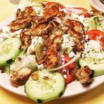 Greek Salad grilled chicken. This picture depicts a salad that it consists of lettuce tomato, peppers, onions, sliced cucumber, feta cheese, chopped grilled chicken and Kalamata olives served on a white platter on Johnys countertop