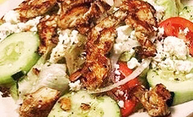 Greek Salad grilled chicken. This picture depicts a salad that it consists of lettuce tomato, peppers, onions, sliced cucumber, feta cheese, chopped grilled chicken and Kalamata olives served on a white platter on Johnys countertop
