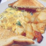 Italian Omelette. This picture depicts an omelette that consists of chopped sausage and peppers, Mozzarella cheese served with home fried potatoes on the side and two slices of white toast cut in half on top of a white plate Served on Johny’s’s counter