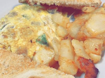 Italian Omelette. This picture depicts an omelette that consists of chopped sausage and peppers, Mozzarella cheese served with home fried potatoes on the side and two slices of white toast cut in half on top of a white plate Served on Johny’s’s counter