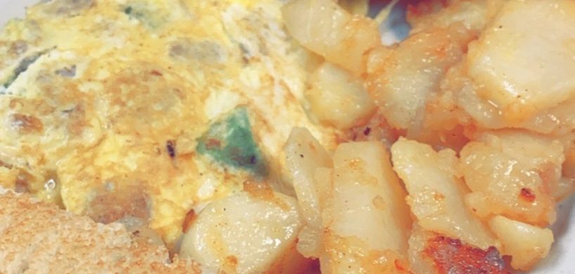 Italian Omelette. This picture depicts an omelette that consists of chopped sausage and peppers, Mozzarella cheese served with home fried potatoes on the side and two slices of white toast cut in half on top of a white plate Served on Johny’s’s counter