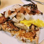 King Kong French toast. This picture depicts French toast made out of eight sub roll that is dipped into the batter. This picture contains the French toast itself topped with Fried eggs, Sliced bananas topped with bacon and ground cinnamon
