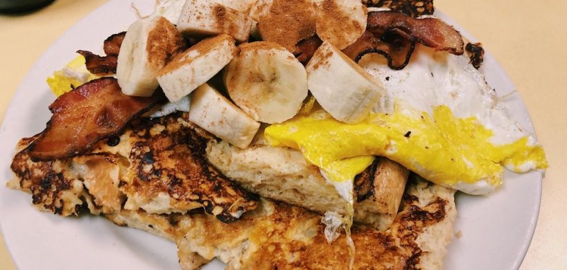 King Kong French toast. This picture depicts French toast made out of eight sub roll that is dipped into the batter. This picture contains the French toast itself topped with Fried eggs, Sliced bananas topped with bacon and ground cinnamon