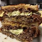 Mr. Moses. Just picture Depicts hot roast beef, homemade coleslaw and melted cheddar cheese on grilled Ryebread that is stacked up one on top of each other on a white platter served on Johnys Luncheonette counter