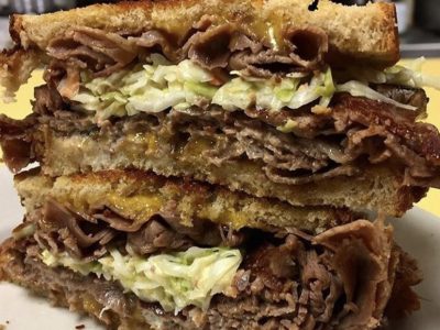 Mr. Moses. Just picture Depicts hot roast beef, homemade coleslaw and melted cheddar cheese on grilled Ryebread that is stacked up one on top of each other on a white platter served on Johnys Luncheonette counter