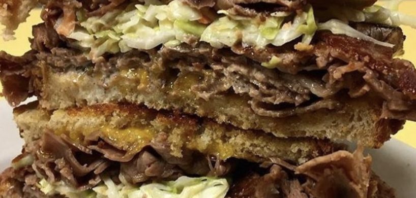 Mr. Moses. Just picture Depicts hot roast beef, homemade coleslaw and melted cheddar cheese on grilled Ryebread that is stacked up one on top of each other on a white platter served on Johnys Luncheonette counter