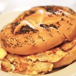Potato and Egg on a Roll. This picture depicts a sandwich that consists of egg and potato combined, on a Kaiser roll that is cut in half on top of a plate Served on Johny’s’s counter top