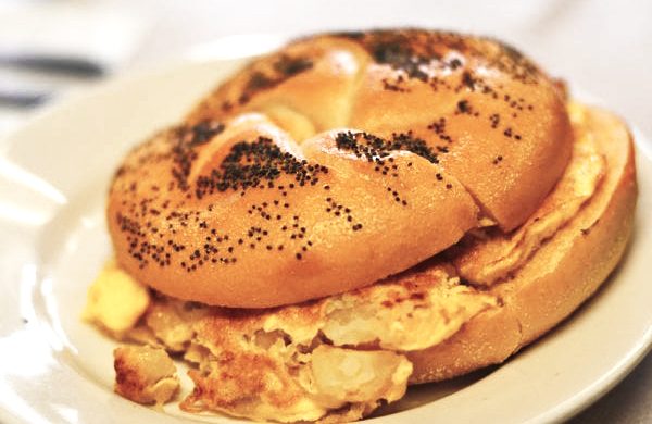 Potato and Egg on a Roll. This picture depicts a sandwich that consists of egg and potato combined, on a Kaiser roll that is cut in half on top of a plate Served on Johny’s’s counter top