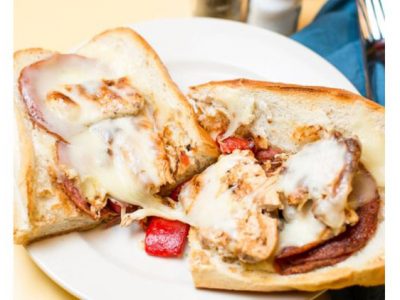The Greco. This picture depicts an order of grilled chicken with roasted red peppers, grilled salami and melted mozzarella cheese that is cut in half and served open face on a white platter serve lunch and he’s going