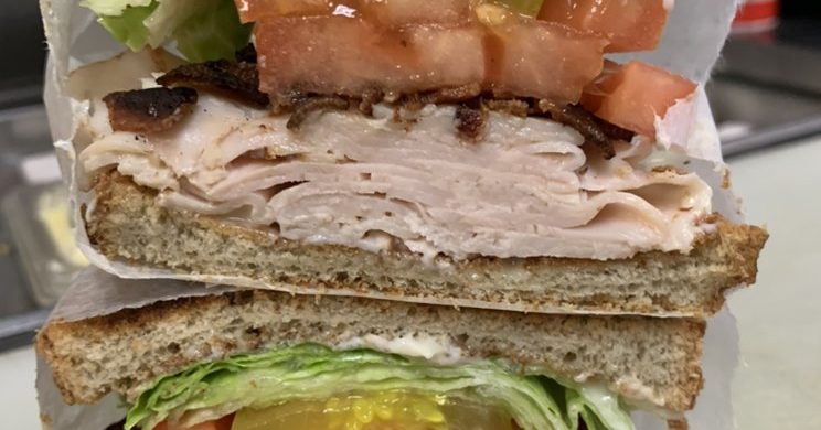 Turkey Club Sandwich. This picture depicts a sandwich that consist of sliced turkey, lettuce and tomato, Bacon Served on Sliced and Toast that is cut in half and placed one on top of another.
