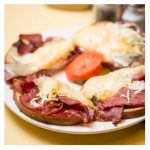 Pastrami Reuben. This picture depicts an order of grilled pastrami, homemade coleslaw Russian dressing and melted Swiss cheese on top of grills Ryebread that is cut into quarters Served open face on a white plaid or on top of Johnys countertop