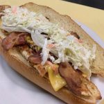 Sloppy Johny. This picture he picks a sandwich on a sub/hero with grilled chicken, raw onion, American cheese, crispy bacon and homemade coleslaw swerved on a white plate on Johnys yellow countertop