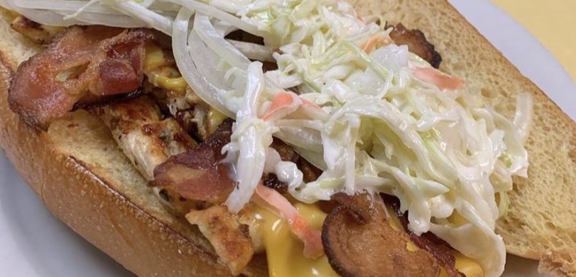 Sloppy Johny. This picture he picks a sandwich on a sub/hero with grilled chicken, raw onion, American cheese, crispy bacon and homemade coleslaw swerved on a white plate on Johnys yellow countertop